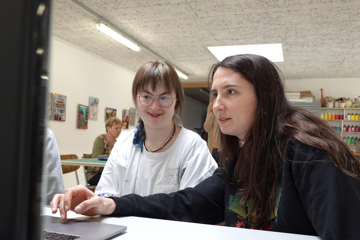 Zwei Personen arbeiten gemeinsam am Computer an einem Plakat.