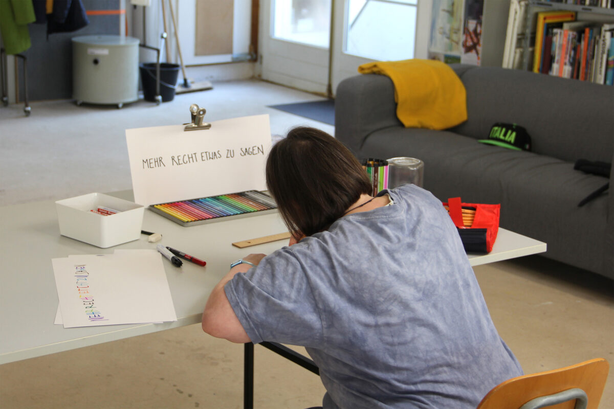 Eine Person schreibt den Text für ihr Plakat mit Filzstiften auf ein Blatt Papier.