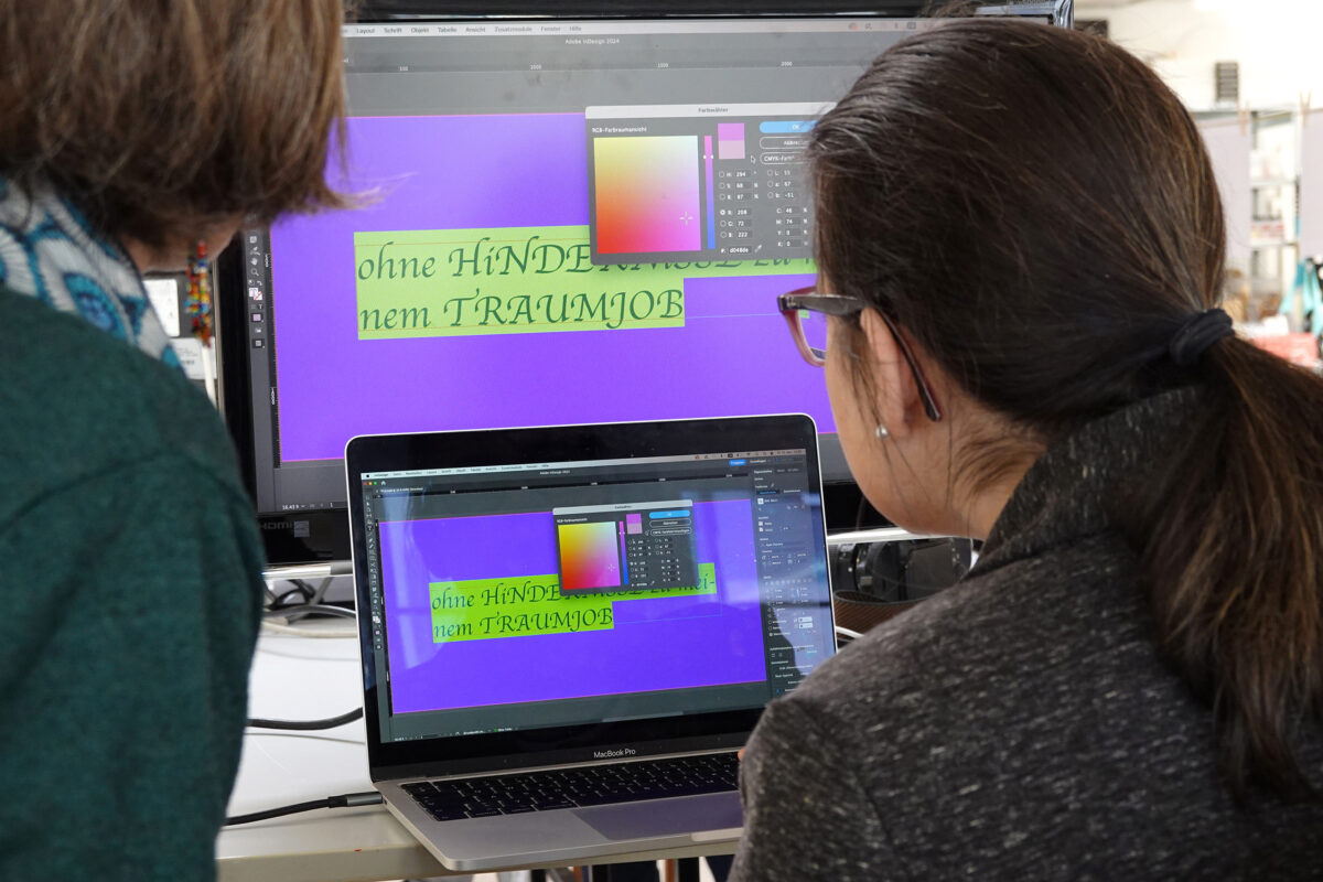 Zwei Personen arbeiten am Computer am Layout eines Plakats.