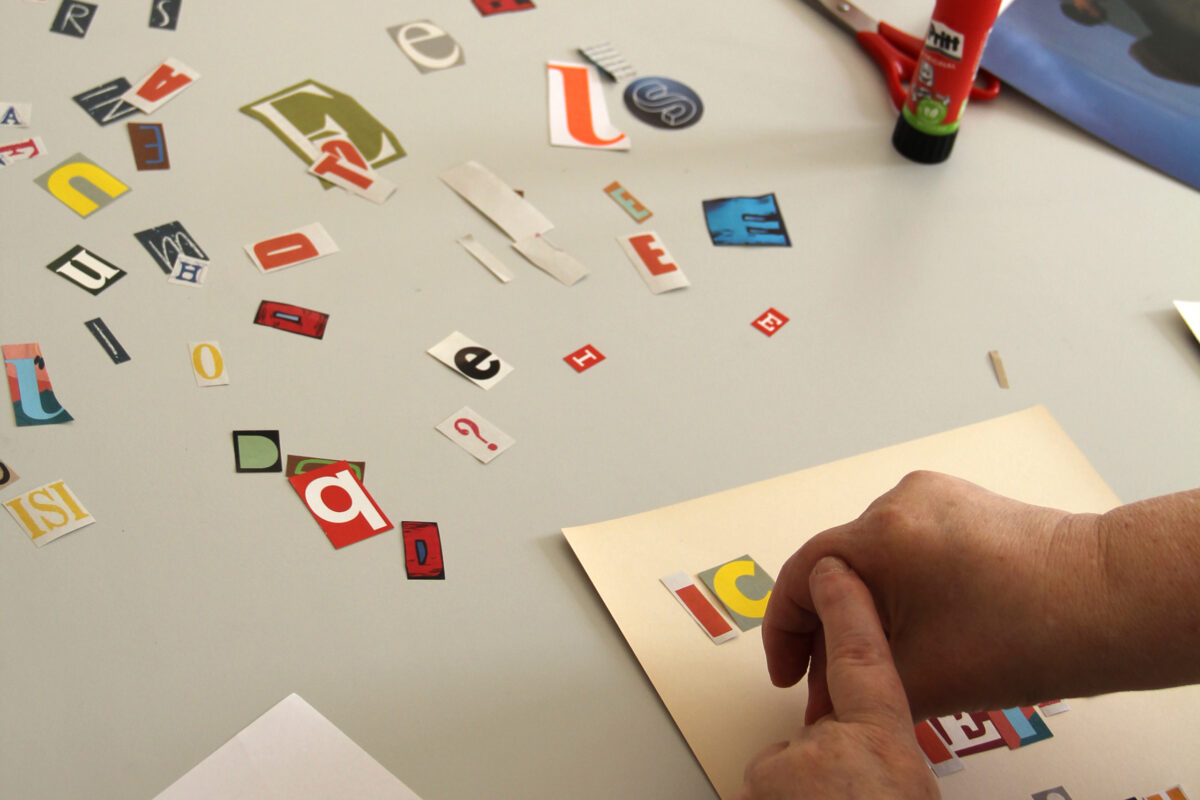 Eine Person klebt den Text für ihr Plakat mit Buchstaben, die aus Zeitschriften ausgeschnitten wurden.