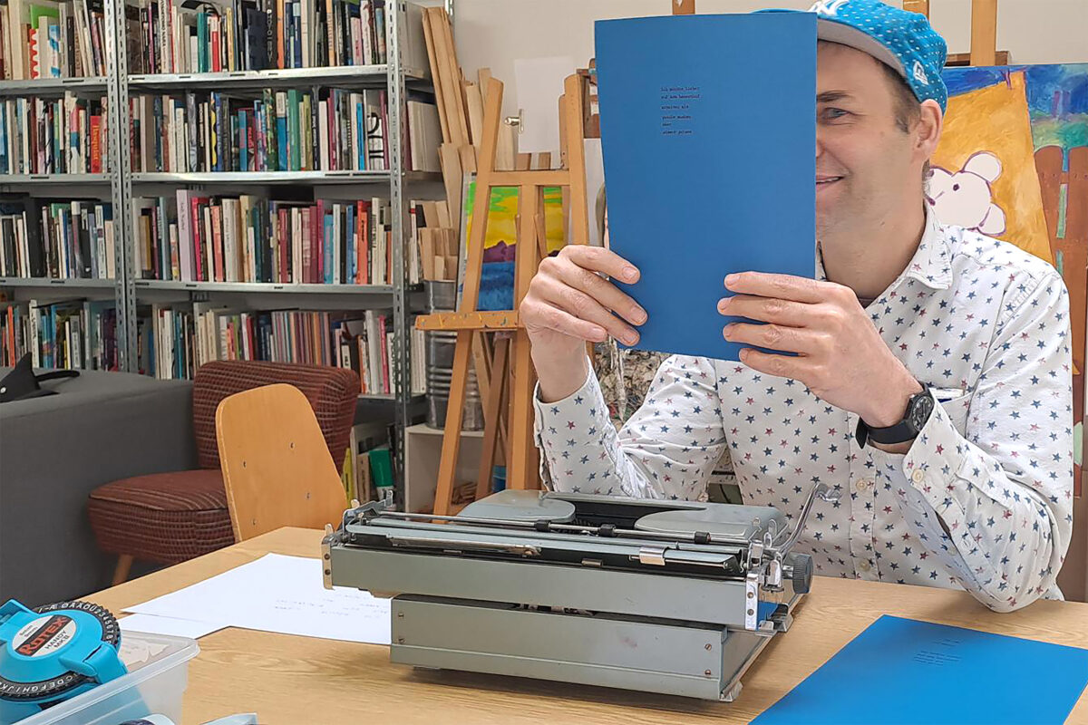 Eine Person hält ein Blatt mit dem auf einer Schreibmaschine getippten Text ihres Plakats mit beiden Händen hoch.